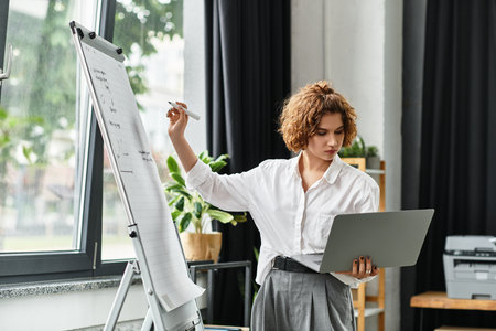 Curly-haired businesswoman collaborates in a bright office, balancing a laptop and notes.の写真素材