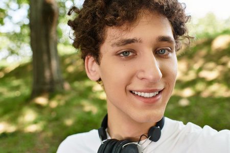 A young man with curly hair smiles while spending time outdoors in a lush green park.の写真素材