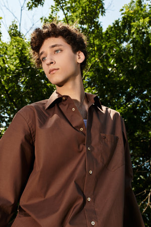 Curly-haired young man embodies summer fashion while relaxing outdoors in a vibrant park.の写真素材