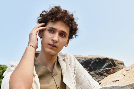 Young man with curly hair embraces summer vibes in a green park, showcasing modern fashion.