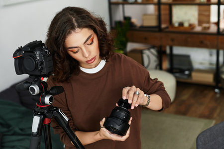 A young woman with curly hair is focused on adjusting her camera lens while working remotely.の写真素材