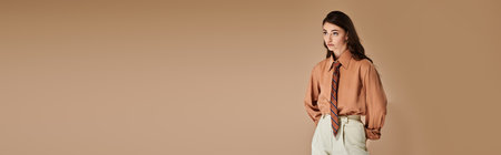 A beautiful young woman with long brown hair showcases a trendy outfit and tie in a studio, bannerの写真素材