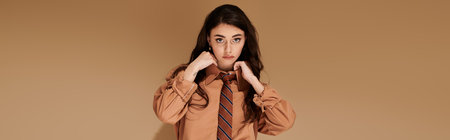 A beautiful young woman with long brown hair exudes confidence in a fashionable attire with tie,...