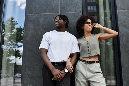 Young couple dressed in trendy outfits smiles and shares a joyful moment in the city on a warm day.の写真素材