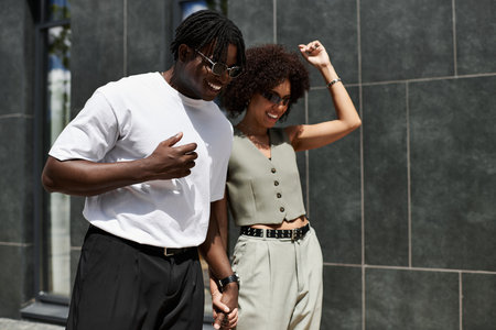 Young African American couple strolls hand in hand, laughing and enjoying urban summer vibes.の写真素材
