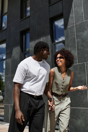 A young African American couple walks hand in hand, sharing smiles on a summer day.の写真素材