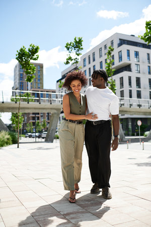Young couple in trendy outfits share joyful moments in the vibrant city streets on a sunny day.