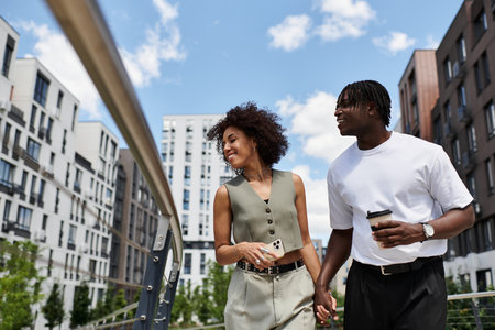 A young African American couple strolls hand in hand through the city, sharing laughter and coffee.の写真素材