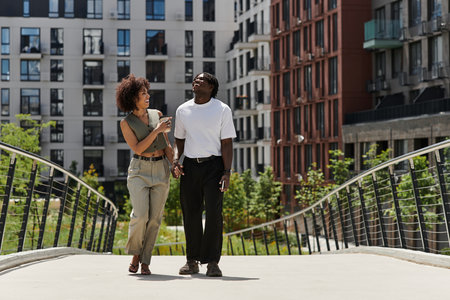 A young African American couple strolls hand in hand, embracing the sunny urban atmosphere.の写真素材