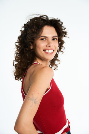 Young woman with curly hair poses confidently in a trendy red tank top, radiating style and joy.