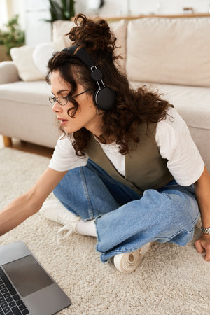 A young woman with curly hair is focused on her laptop while working remotely at home.