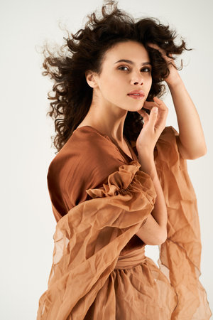 A captivating young woman with curly hair poses in a flowing dress against a grey backdrop.の写真素材