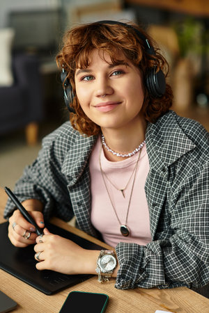 Young woman with curly hair focuses on her graphic tablet while enjoying remote work in her cozy...