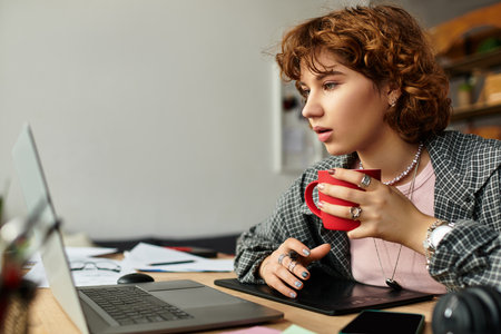 Young woman with curly hair engages in remote work from her stylish home, enjoying coffee.の写真素材