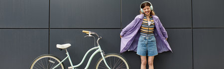 A joyful young woman stands beside her bicycle wearing stylish summer clothes and headphones.