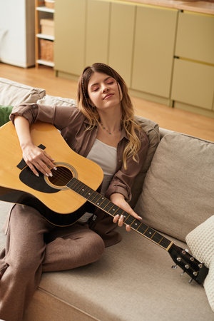 Beautiful woman relaxes on a couch, strumming her guitar and embracing a joyful summer vibe.