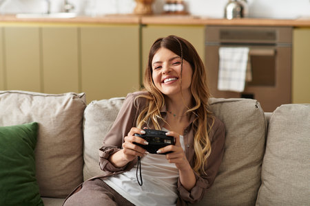 A beautiful young woman smiles while holding a retro camera, embracing summer vibes indoors.の写真素材