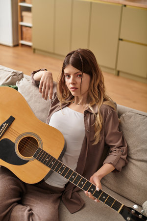 A young woman relaxes on a comfy sofa, strumming her guitar and soaking in summer vibes.