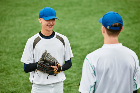Two young boys share a light moment while playing baseball on a vibrant green field.