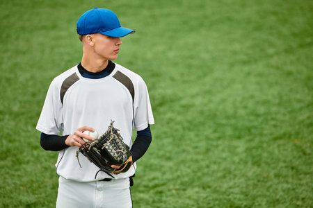 A confident player stands ready on a vibrant baseball field, holding a glove and ball.の写真素材