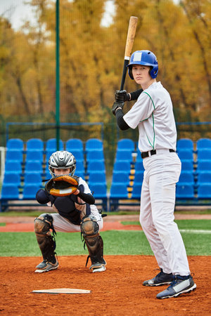 Two teenage boys play baseball on a vibrant field surrounded by autumn foliage.