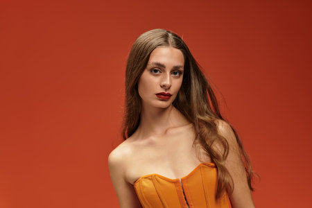 A striking young woman poses confidently in a bright orange corset, exuding charm and grace.の写真素材