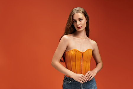 A young beautiful woman confidently demonstrates her style in an orange top paired with jeans.の写真素材