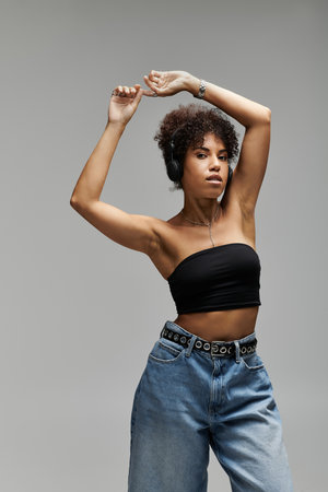 A fashionable woman showcases her trendy outfit while dancing energetically against a grey backdrop.の写真素材