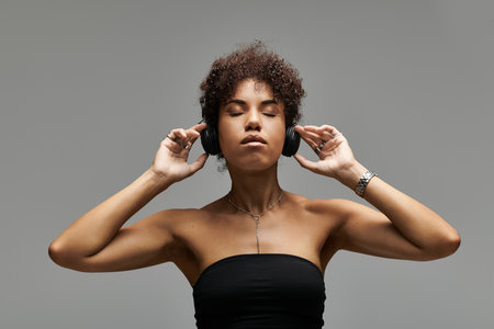 A trendy african american woman enjoys music while wearing stylish headphones on a grey background.の写真素材