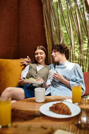 Loving couple shares laughter and sweet snacks while relaxing together in a tranquil park.の写真素材