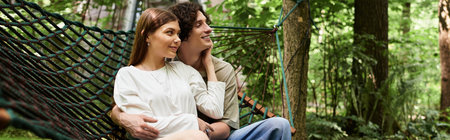 In a tranquil park setting, a young couple shares loving smiles while relaxing on a hammock.の写真素材