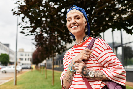 Joyful young woman in a park exuding confidence, showcasing her tattoos and trendy outfit.の写真素材