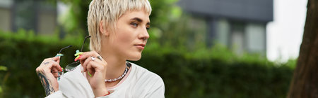 A young beautiful woman sits gracefully in the park, reflecting while holding glasses.の写真素材