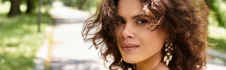 In a vibrant green park, a young woman with curly hair enjoys a sunny day, bannerの写真素材