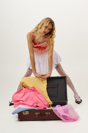 Stylish young woman showcases outfits beside a vintage suitcase, creating a vibrant vibe.の写真素材