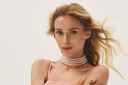 Blonde woman with a stylish pearl choker and flowing hair showcases her beauty in a trendy space.の写真素材