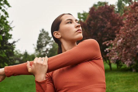 A young and athletic woman engages in a yoga stretch amidst lush greenery and vibrant trees.の写真素材