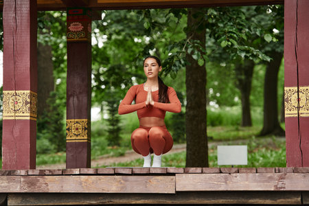 A young woman practices yoga in nature, showcasing strength and balance in a serene environment.の写真素材