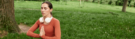 Serene woman engages in yoga practice, fostering inner peace among lush grass and trees.の写真素材