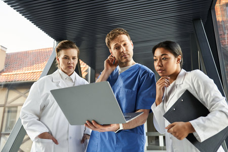 Three multicultural doctors discuss patient care options while reviewing information on a laptop.の写真素材