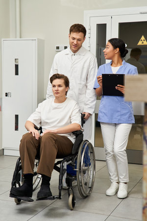 Handsome doctor and nurse support a female patient in a wheelchair before MRI scan.の写真素材