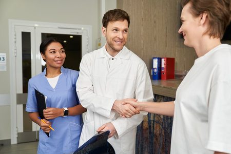Handsome doctor shaking hands with female patient near smiling nurse in clinicの写真素材