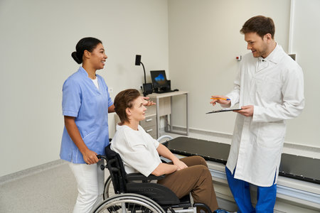 Care team assists female patient in a wheelchair for an MRI scan at a modern facility.の写真素材
