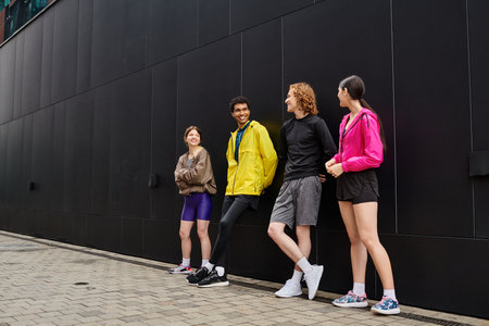 Four sporty young individuals engage in lively conversation while leaning against a modern wall.