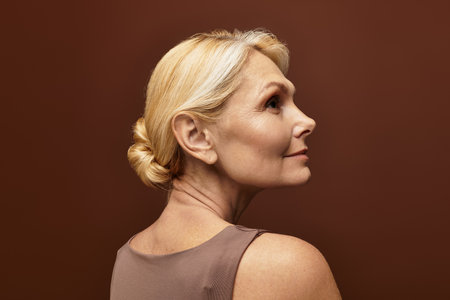A senior beautiful woman gazes thoughtfully, highlighting her elegance against a warm background.