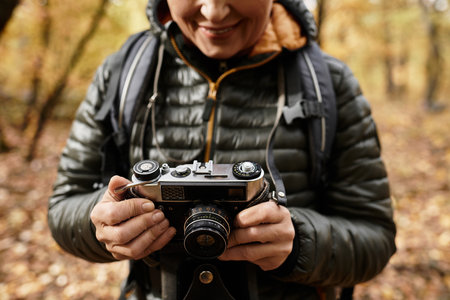 Senior woman enjoys nature while taking photos in a colorful forest landscapeの写真素材