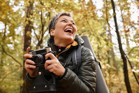 Senior woman laughs heartily as she captures memories with her camera on a forest hike.