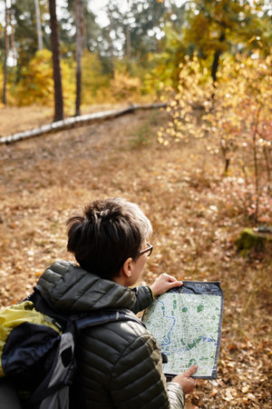 Senior woman enjoys a peaceful hike in the forest, studying her map among falling leaves.の写真素材