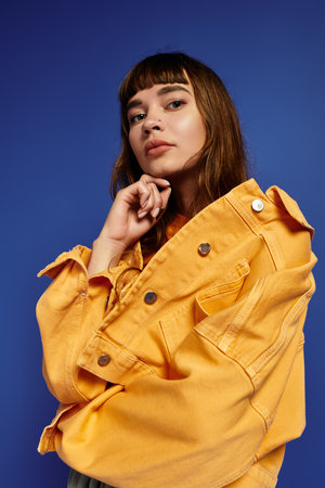Confident young woman showcases her fashionable attire with a striking pose against blue background.