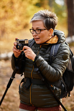 Hiking through a colorful forest, a senior woman enjoys taking pictures of natures beauty.の写真素材